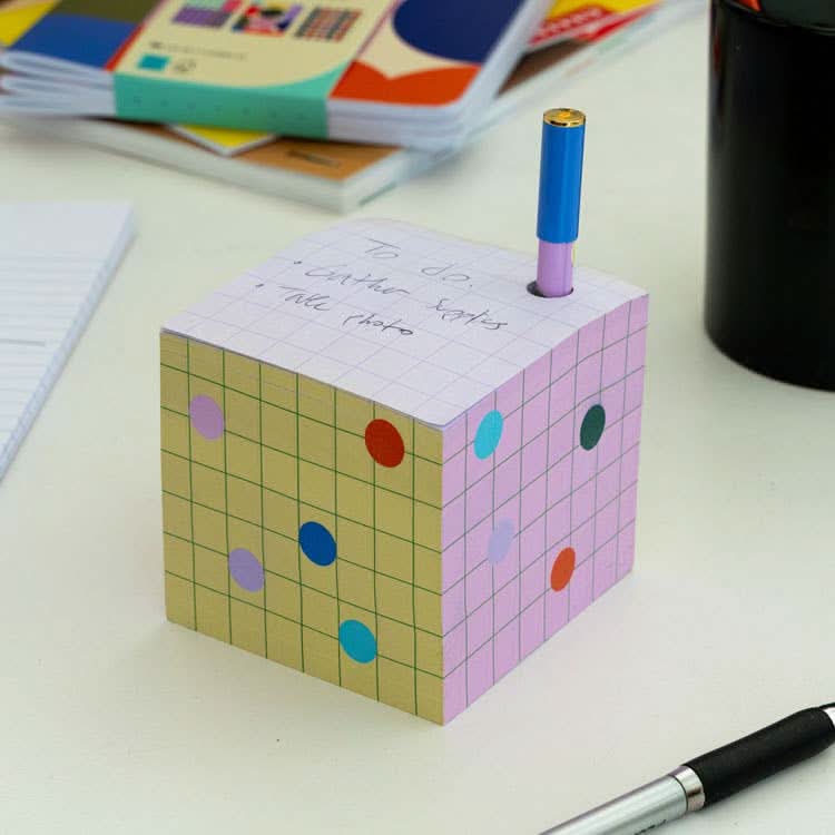 Colorful sticky note block with a hole to contain pen sitting on a desk