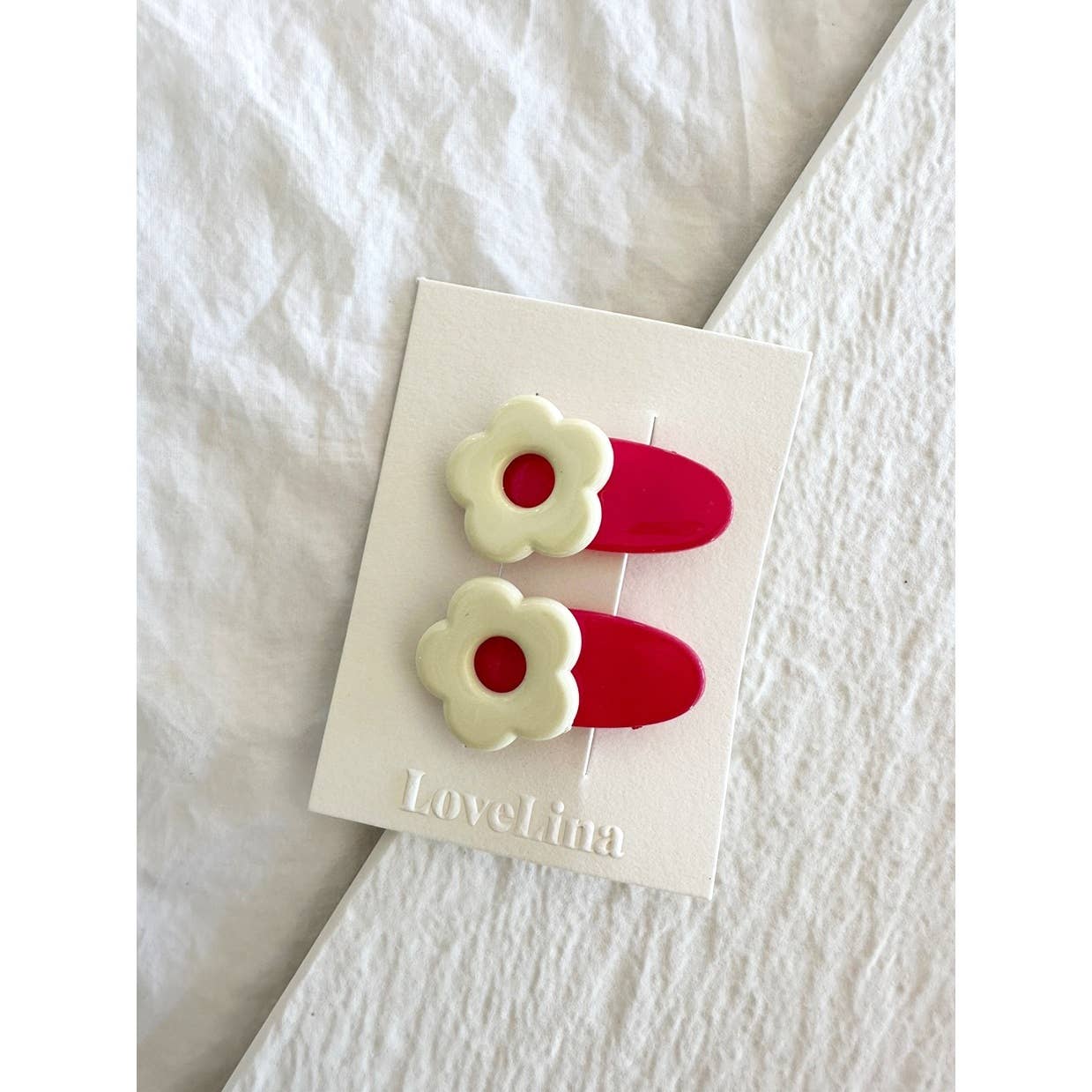 Pair of mini white and red flower clips clipped to display card laying on white cloth