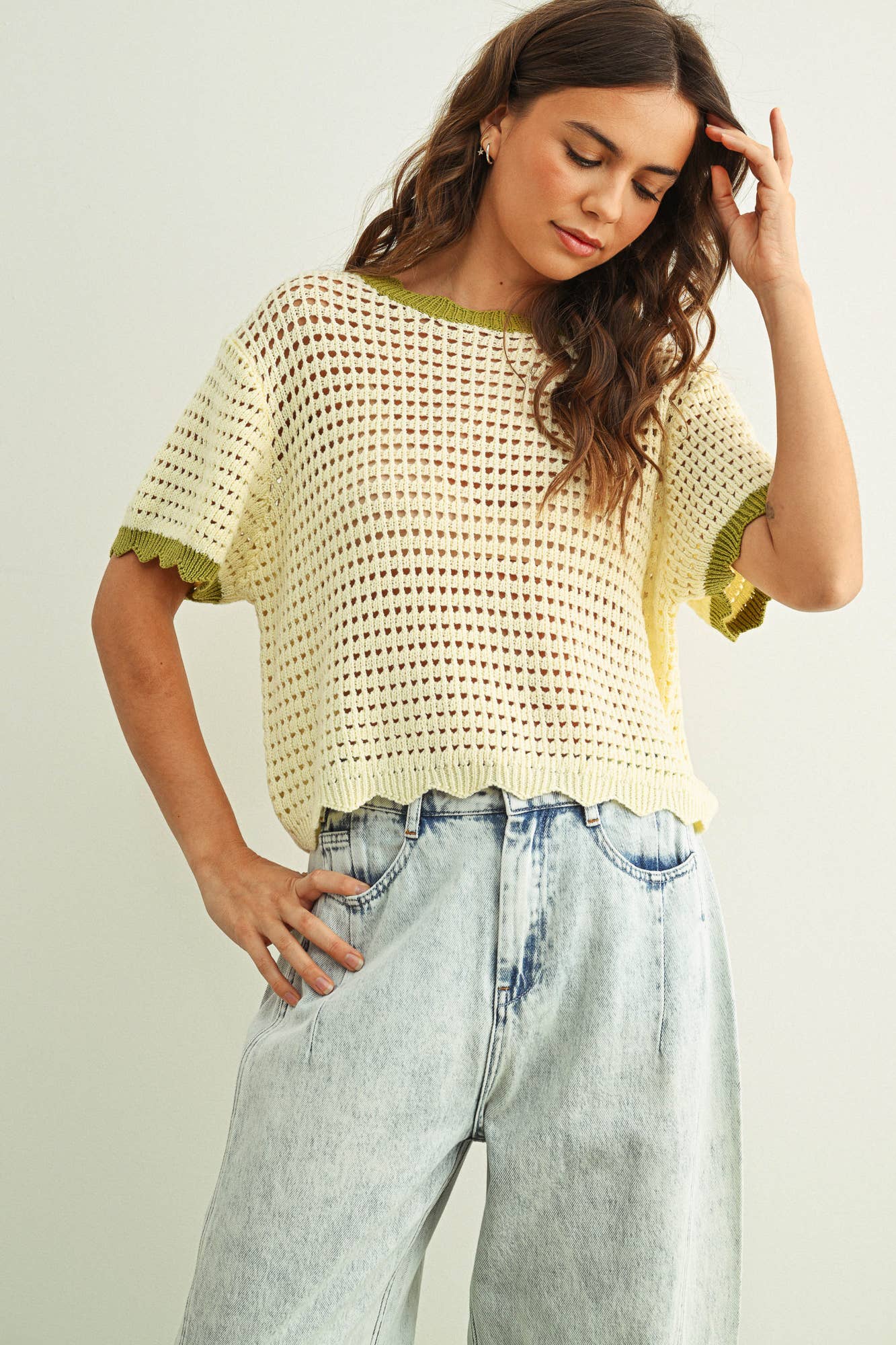 Woman wearing a yellow crochet top and light blue jeans against a plain background