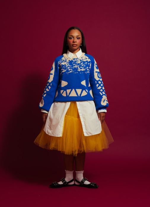 Woman wearing royal blue and white knit sweater with white oversized dress shirt underneath paired with a mustard yellow tulle skirt 