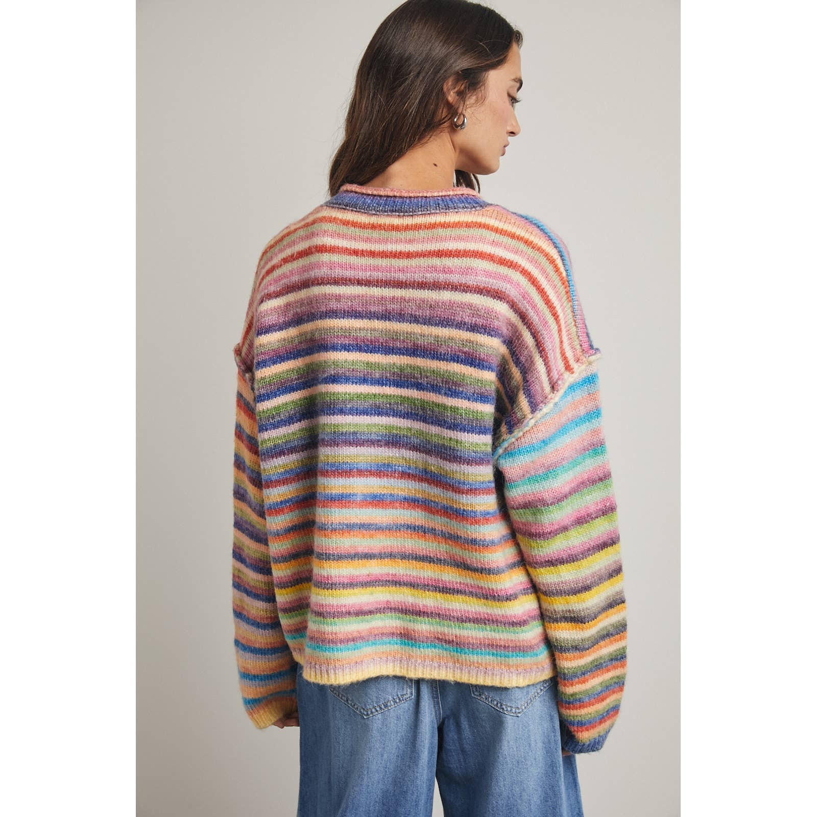 Person wearing a colorful striped sweater and blue jeans against a plain background