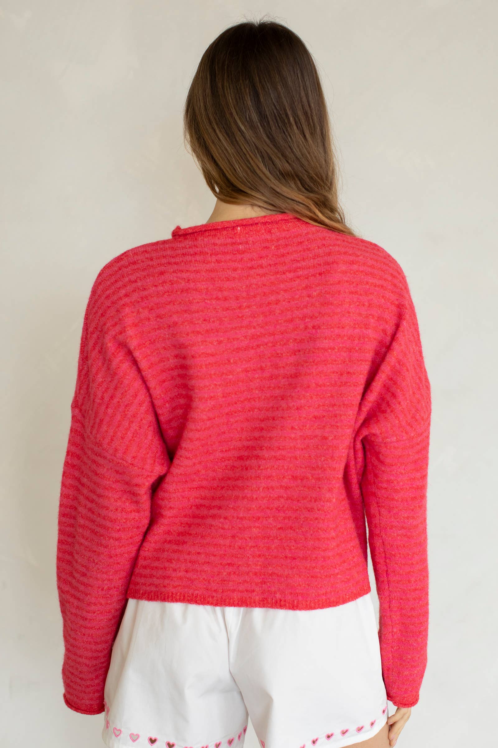 Person wearing a red textured sweater and white pants against a plain background