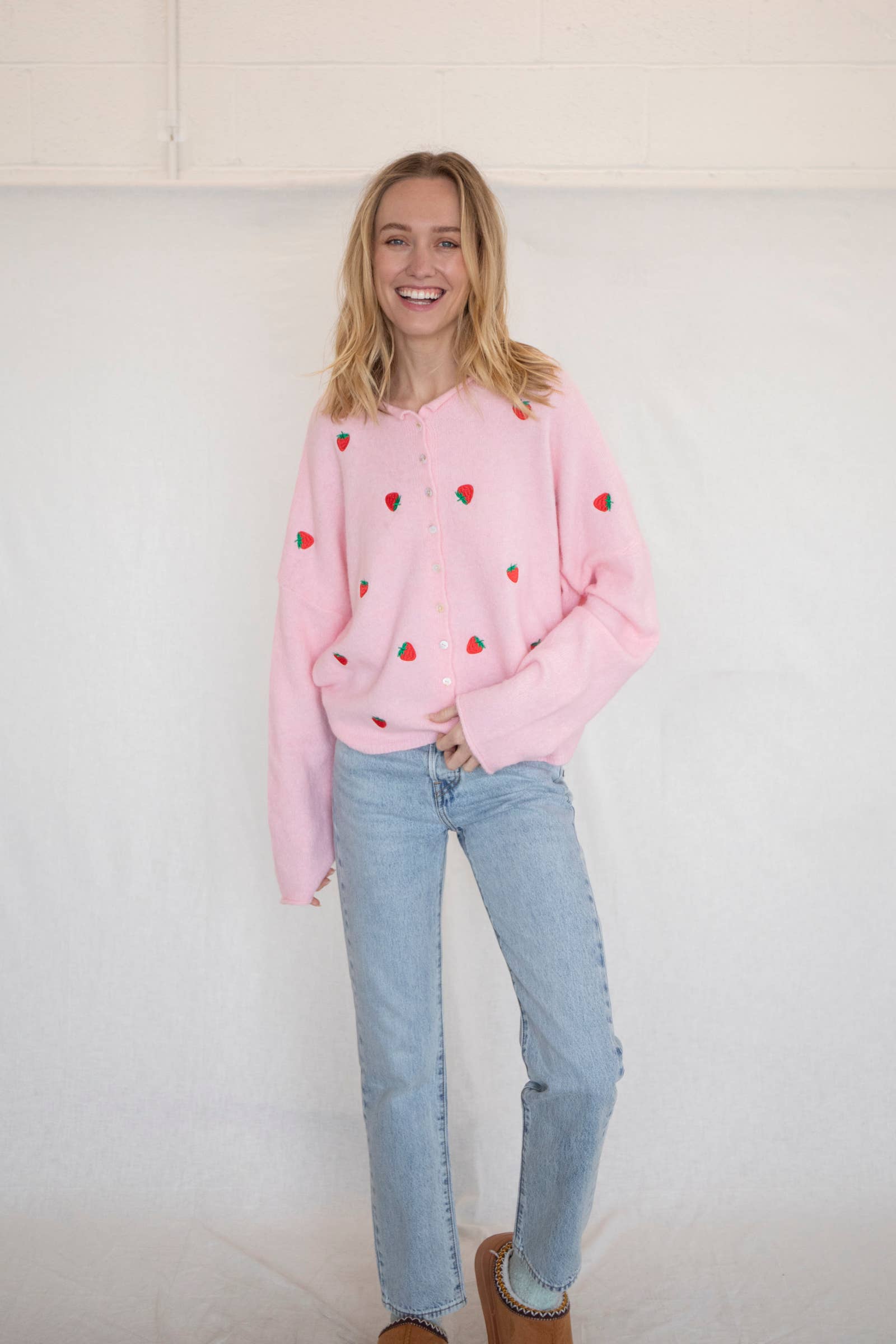 Woman wearing a pink button down cardigan with strawberries and blue jeans