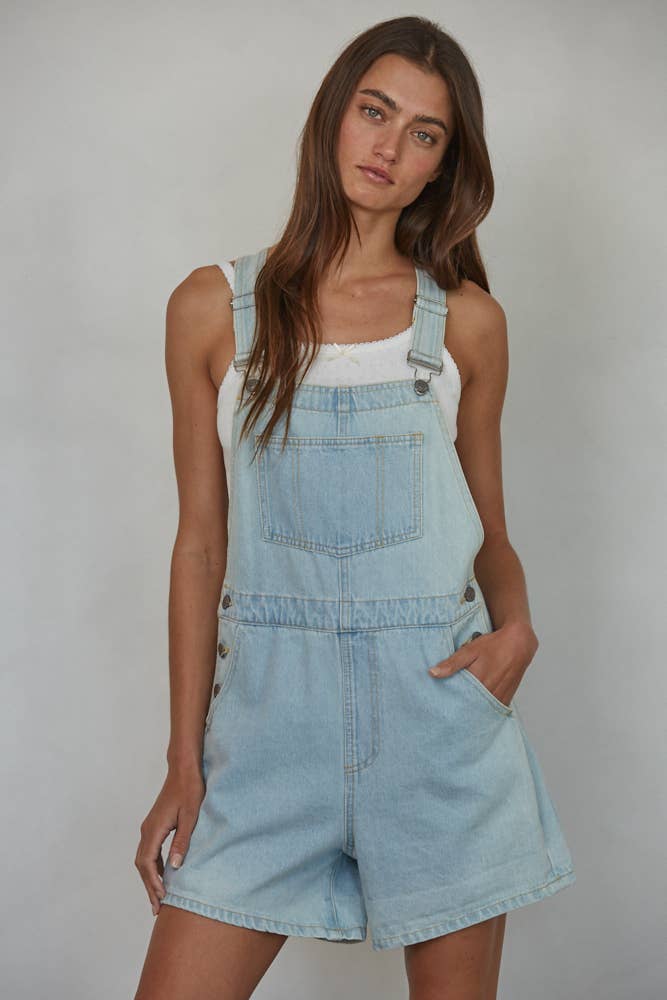 Woman wearing light blue denim overalls against a plain background