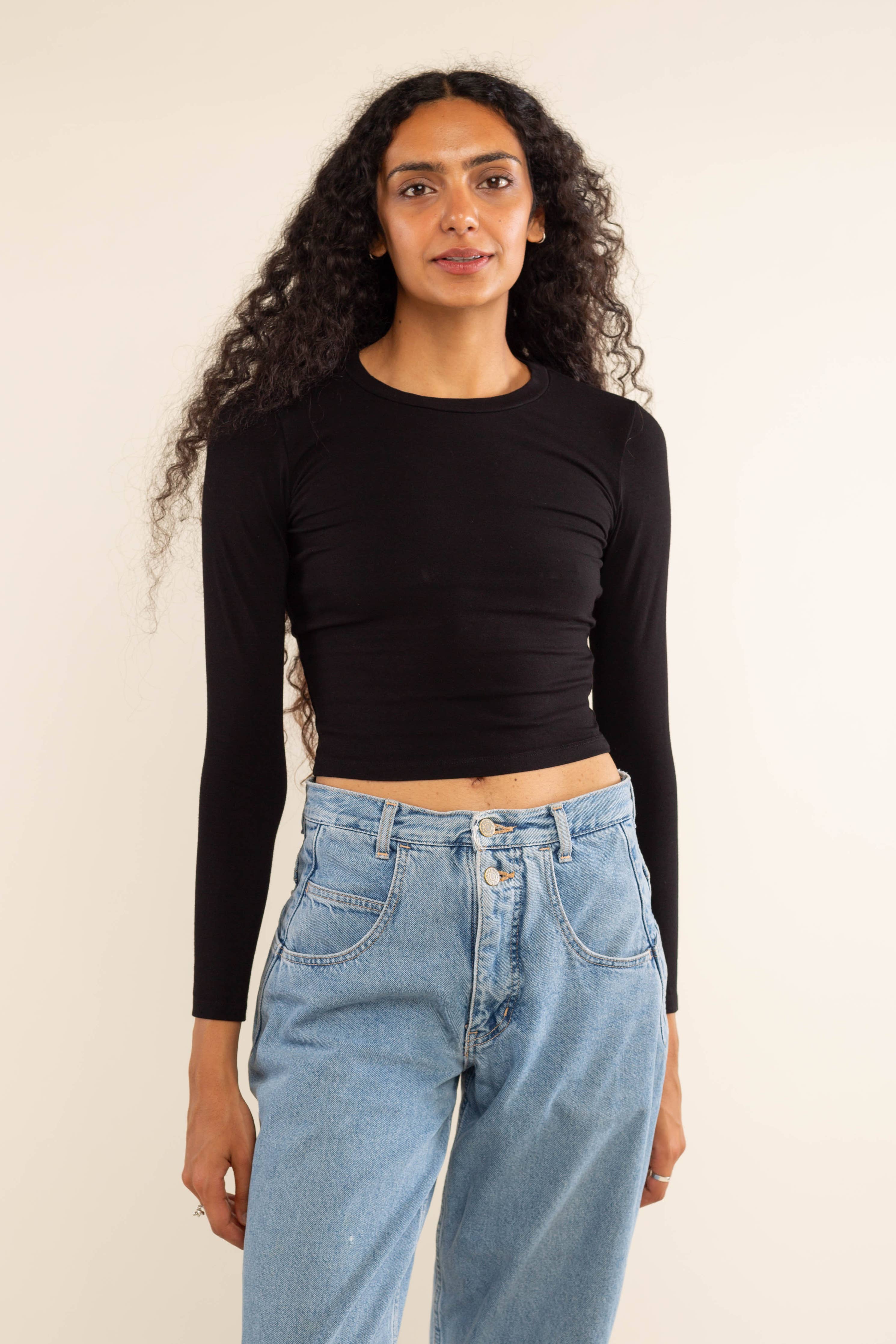 Woman wearing white, long sleeve, tight, crew neck, top with blue jeans