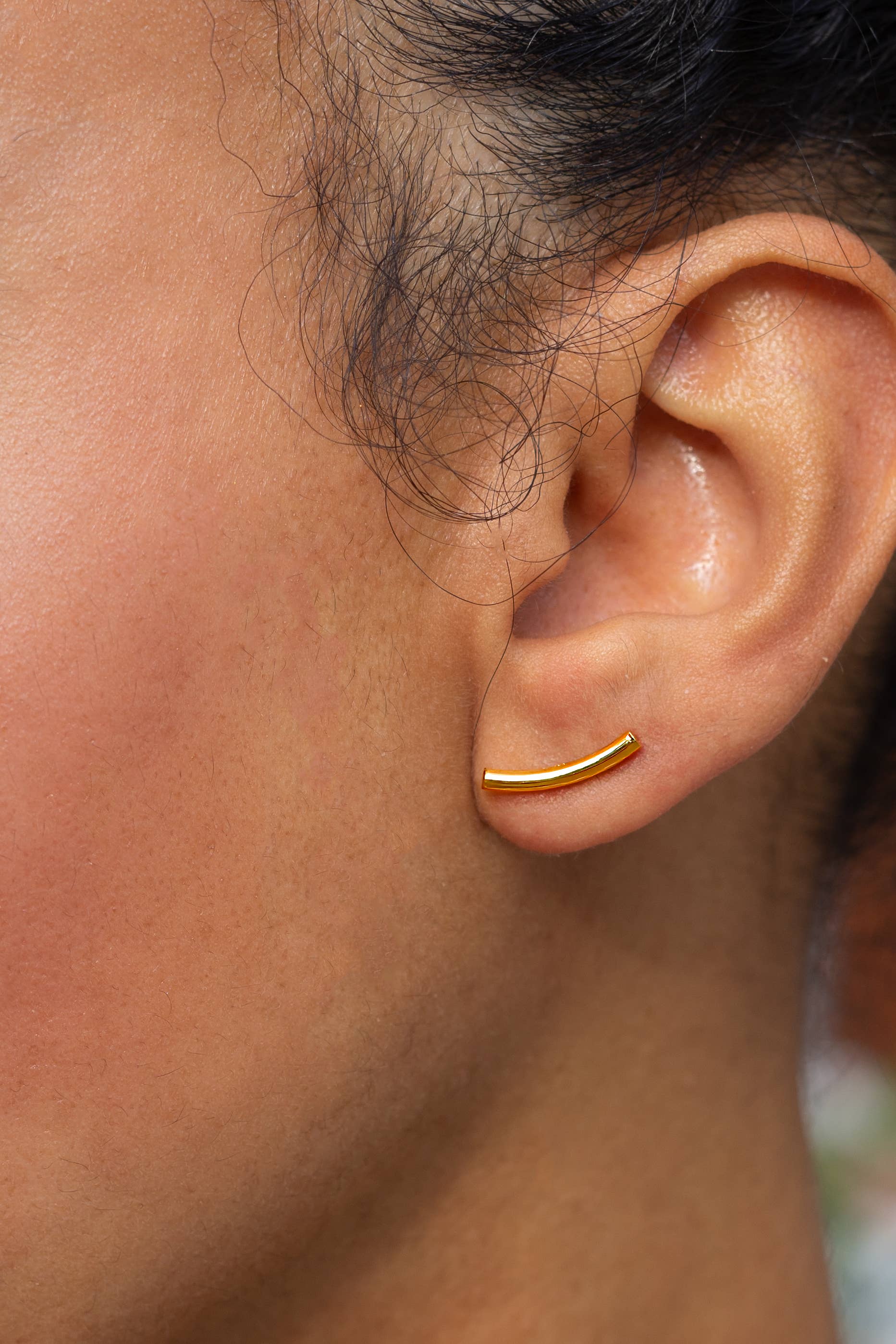 Close-up of an ear wearing a gold hoop earring with blurred background