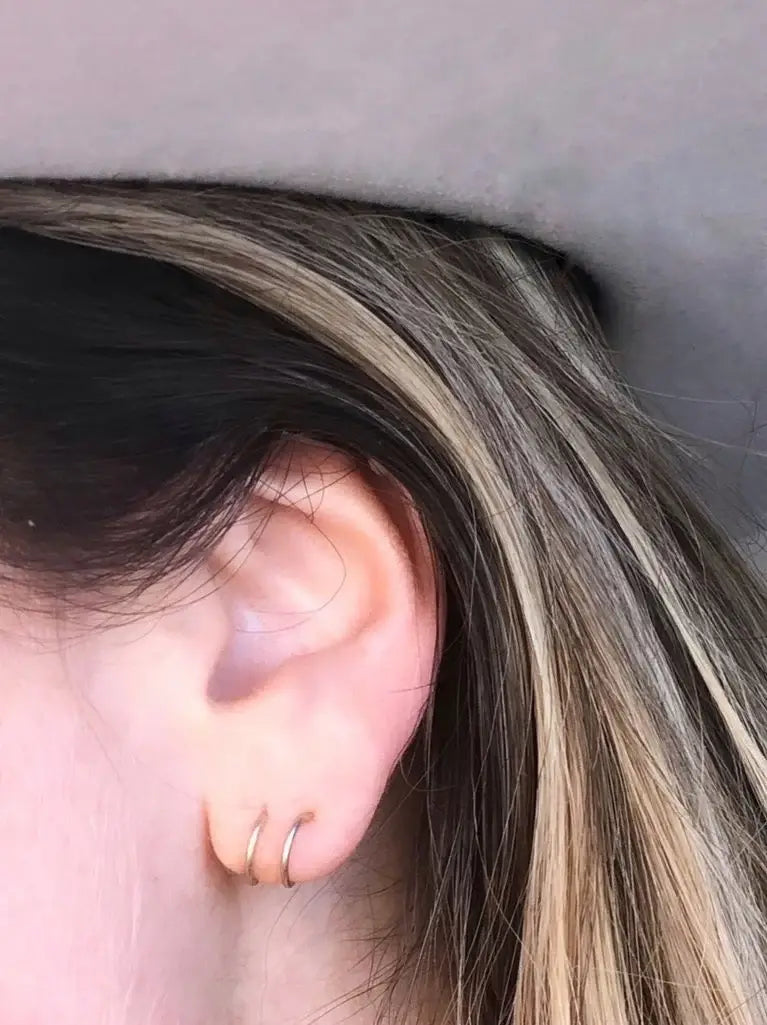 Close-up of an ear with a gold hoop earring against a neutral background