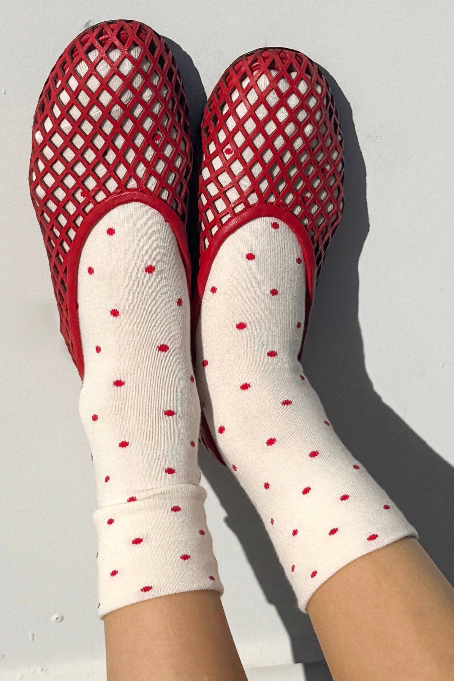 Red mesh sandals and white socks with red polka dots on a light gray background