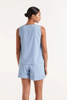 Woman wearing  blue denim like sleeveless  button down top and matching shorts