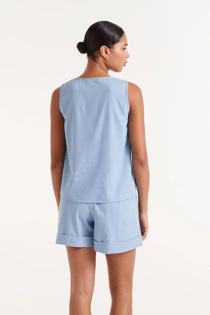 Woman wearing  blue denim like sleeveless  button down top and matching shorts