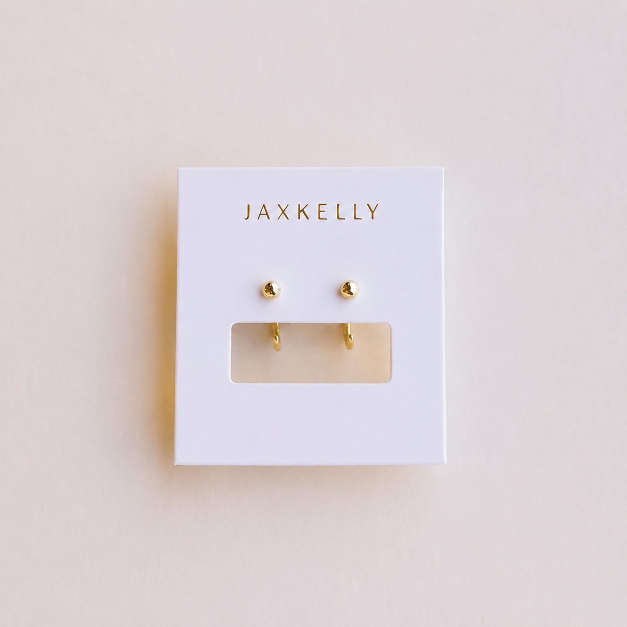 Gold earrings on a Jaxkelly branded card against a beige background