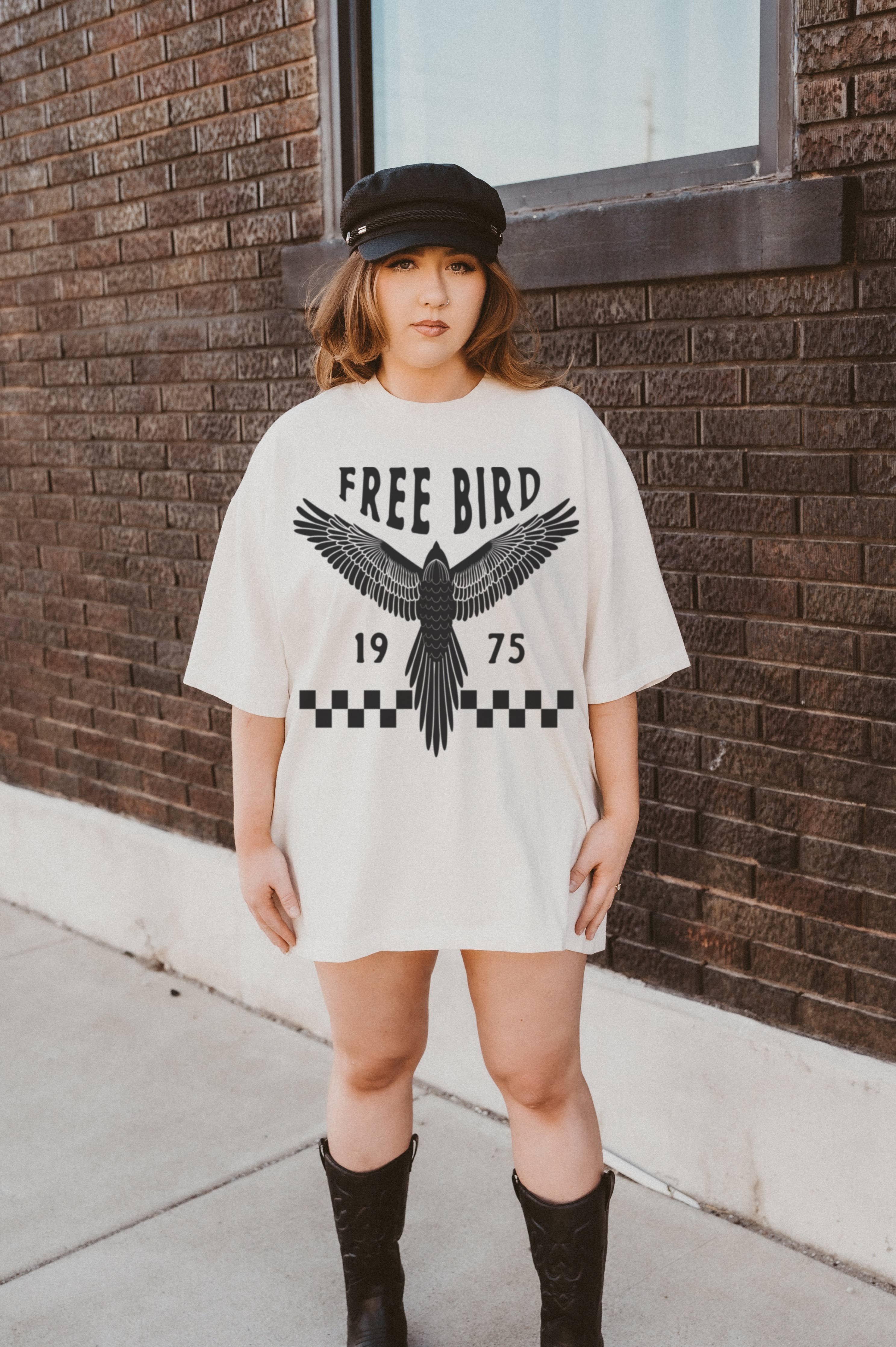 Person wearing a white t-shirt with 'Free Bird' design against a brick wall.