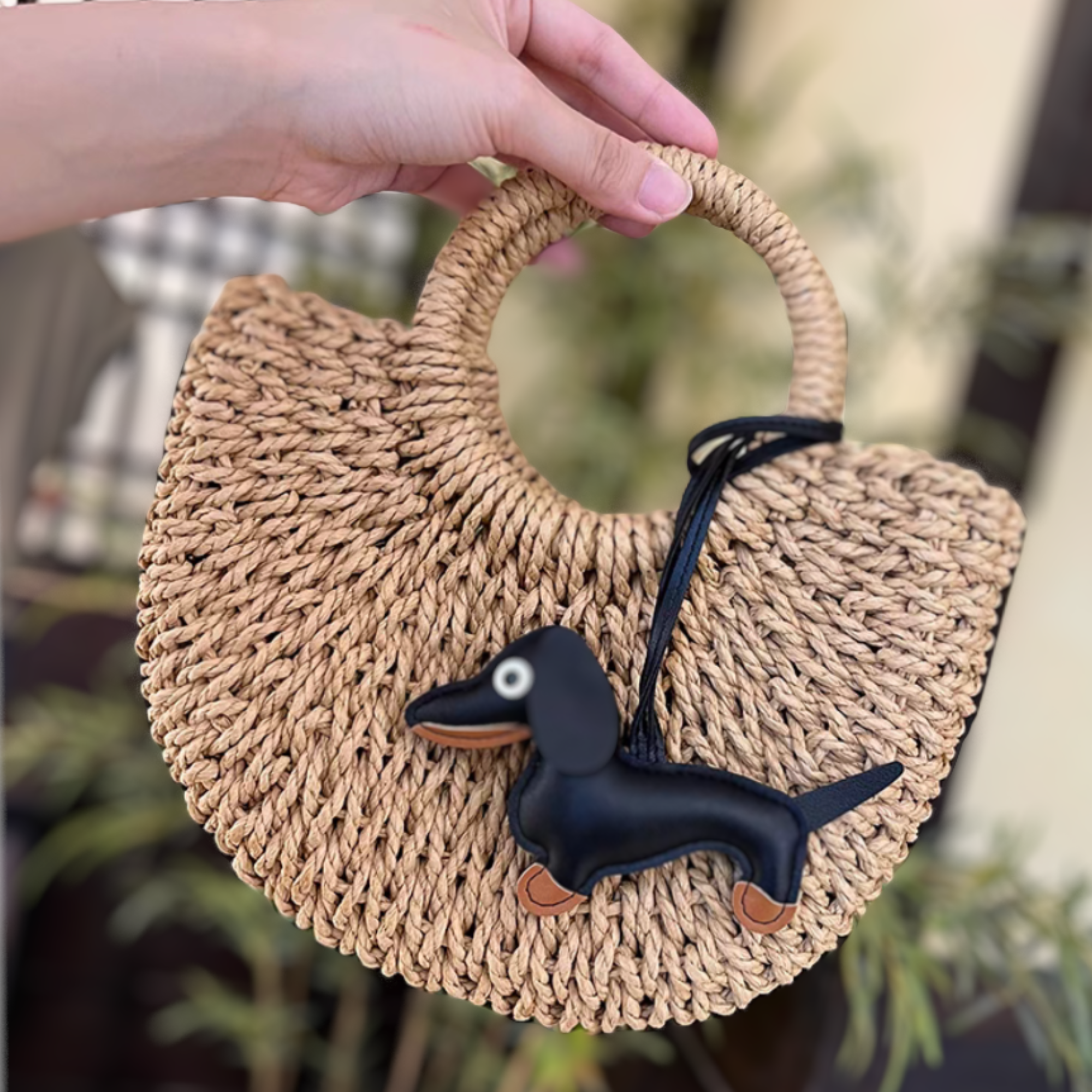 A black Dachshund Leather Bag Charm shown attached to a tan woven handbag 