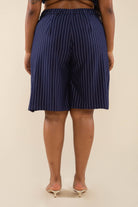 Woman wearing navy vertical pin striped knee length shorts and white heels behind a blank background. 