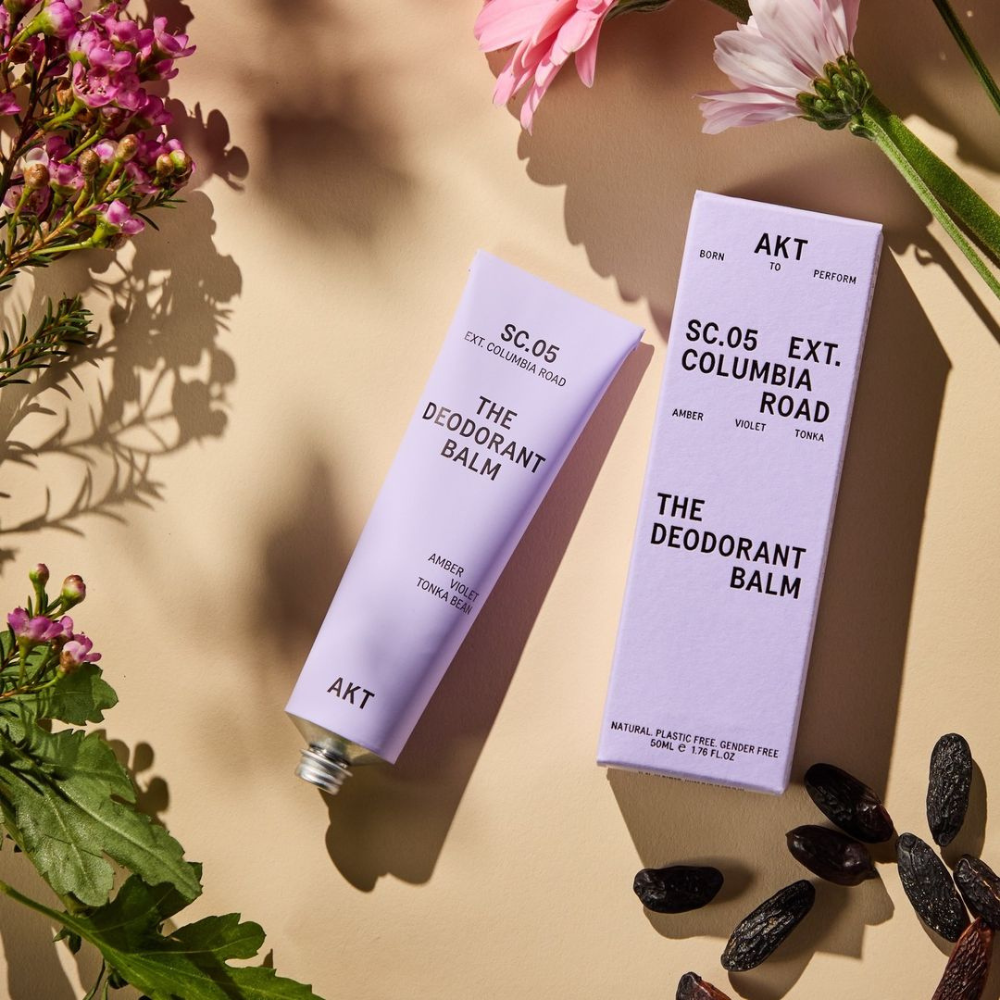 deodorant balm in a lavender tube laying on a table next to lavender color packaging 