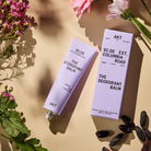 deodorant balm in a lavender tube laying on a table next to lavender color packaging 