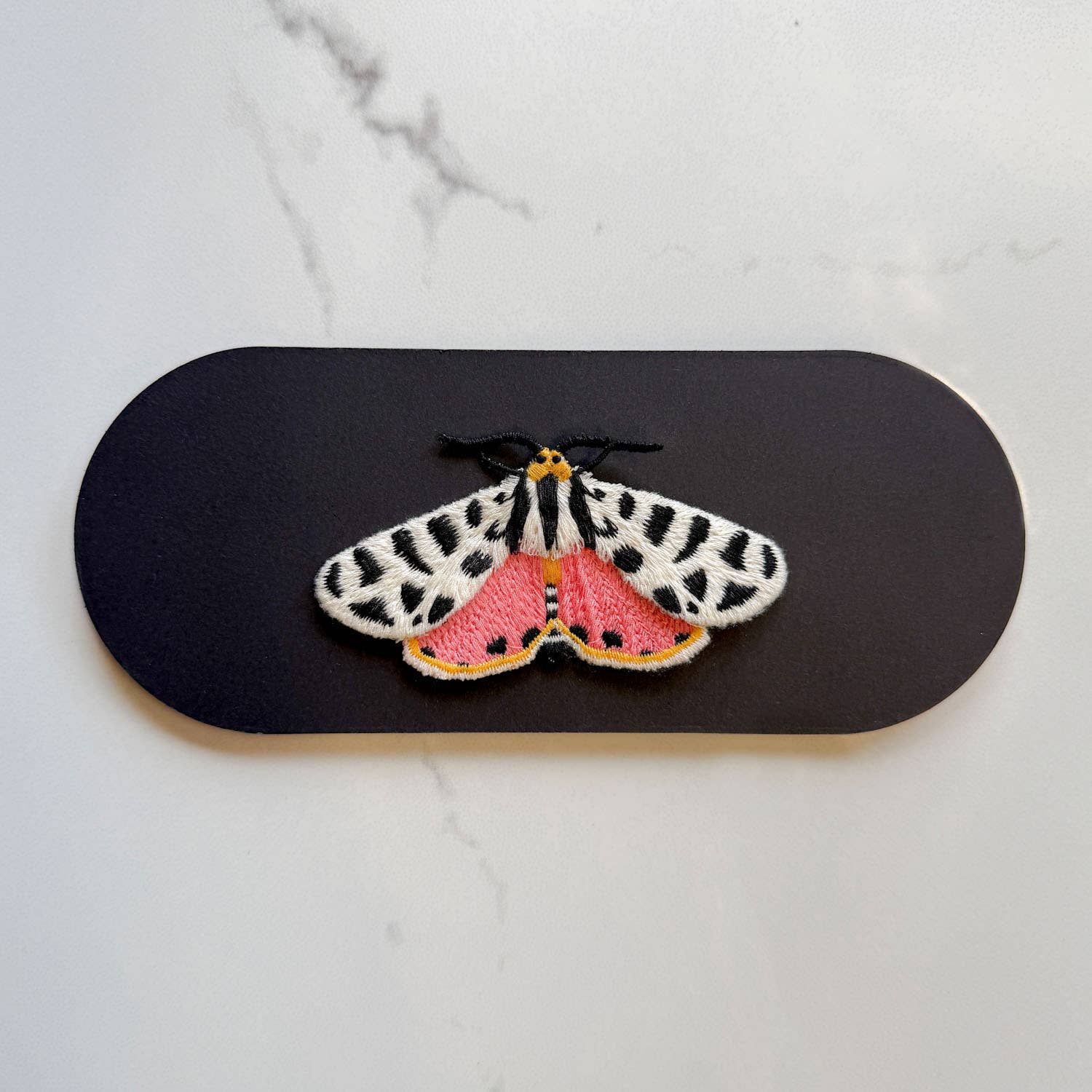 Embroidered butterfly patch on a black card with a white marble background