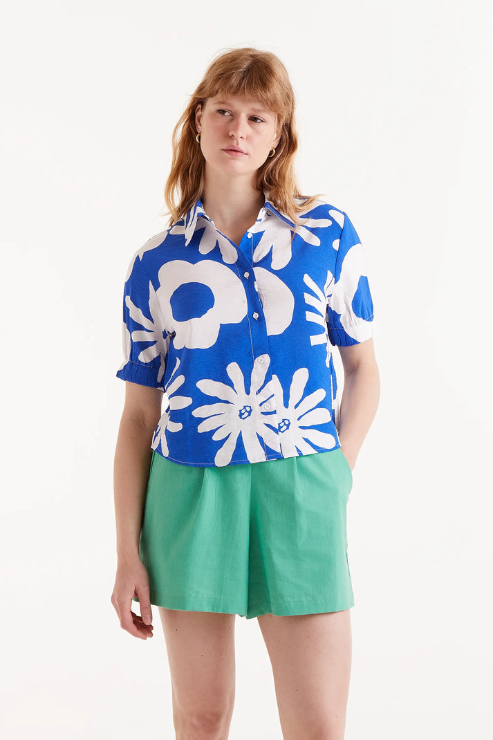 Woman wearing large print button up blouse in blue and white paired with green shorts 