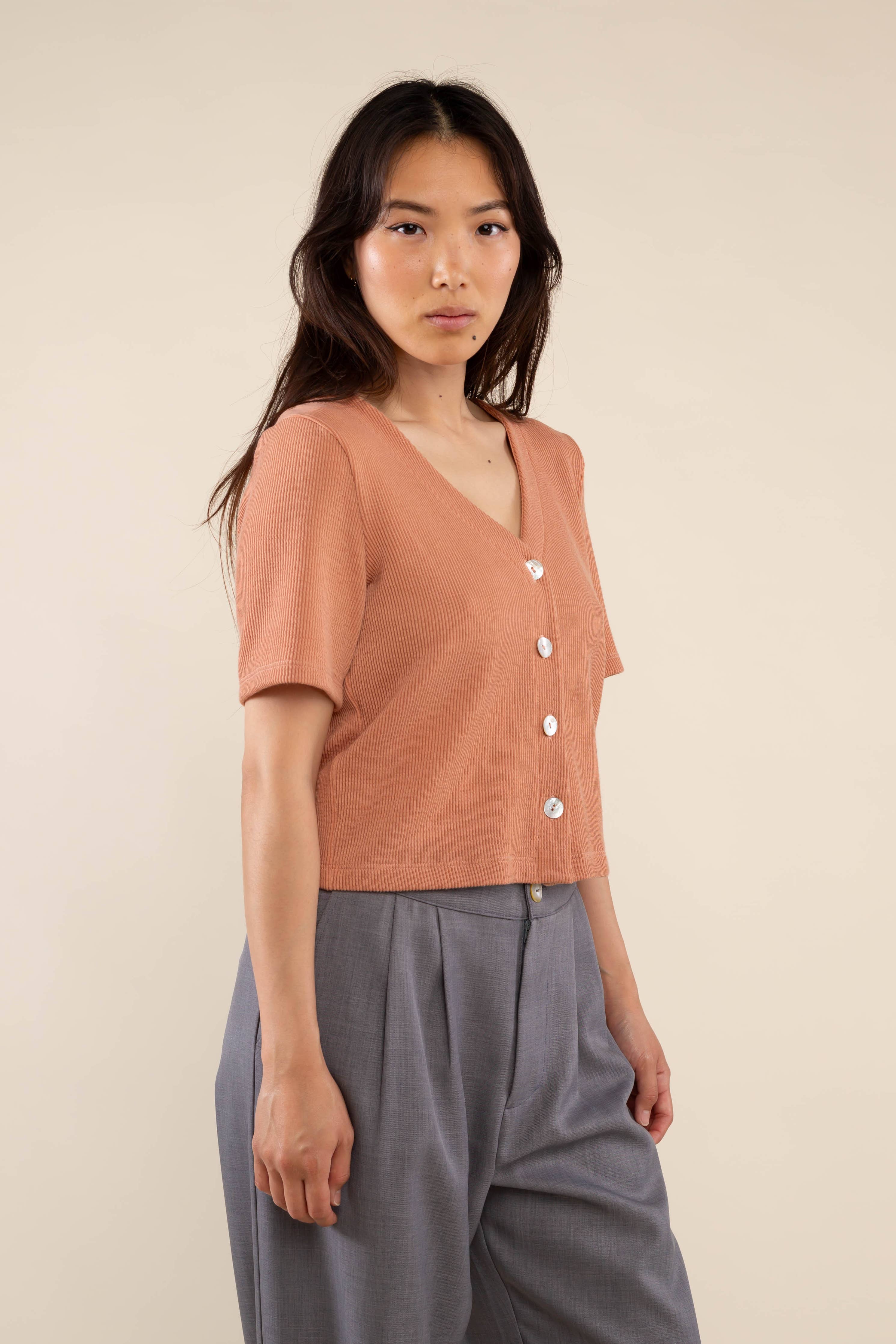 Woman wearing brick colored, ribbed, button down, short sleeve blouse top and grey pants 