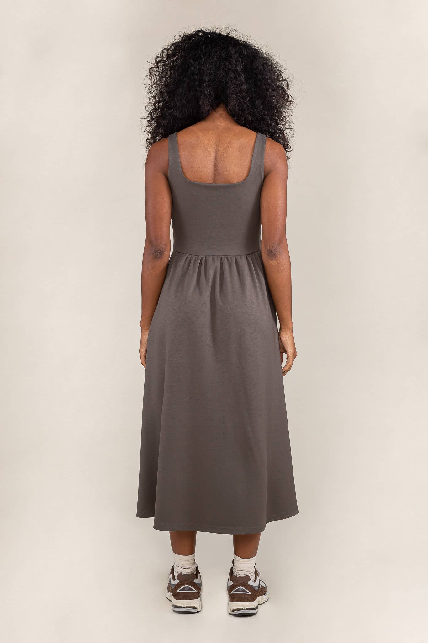 Woman facing away from the camera wearing olive colored, midi dress, with corset bodice detail