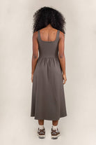 Woman facing away from the camera wearing olive colored, midi dress, with corset bodice detail