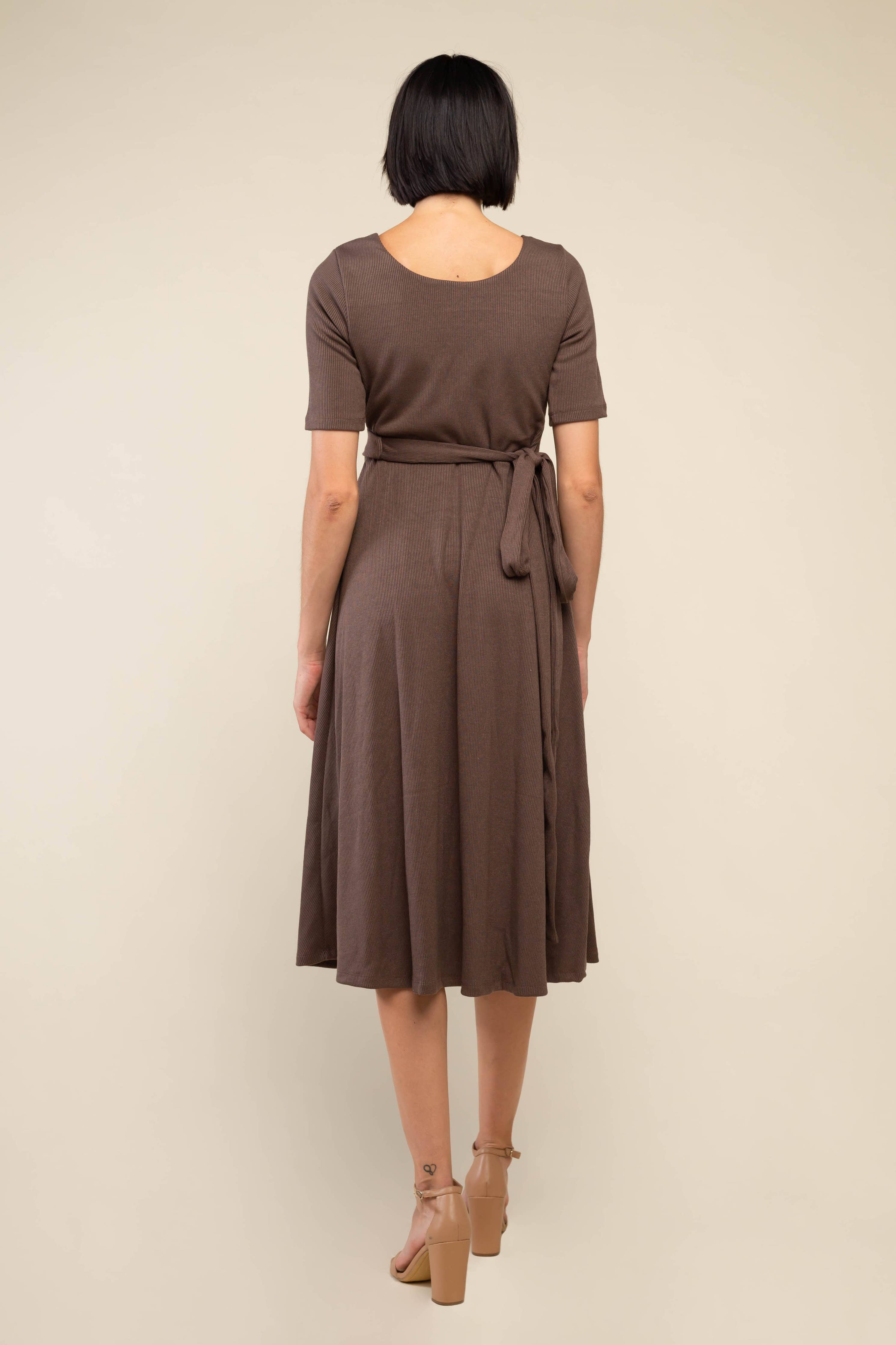 Woman facing away from the camera wearing high heels and brown midi ribbed dress with waist adjustable tie at waist
