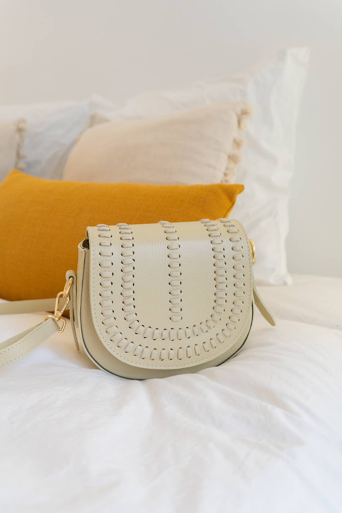 Cream colored leather crossbody bag with magnetic front clap and leather woven geometric details 