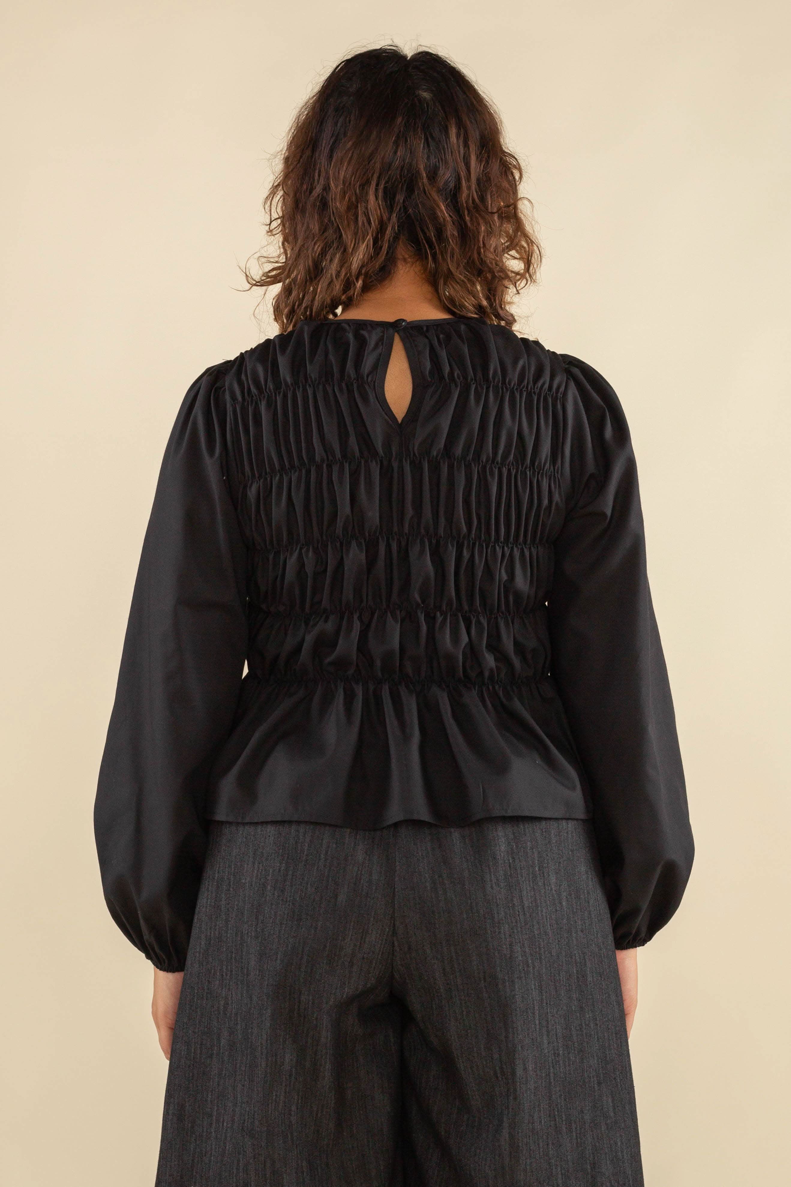 Woman facing away from the camera wearing black, bubble long sleeve, shirred, peplum style top with back eye detail
