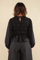 Woman facing away from the camera wearing black, bubble long sleeve, shirred, peplum style top with back eye detail