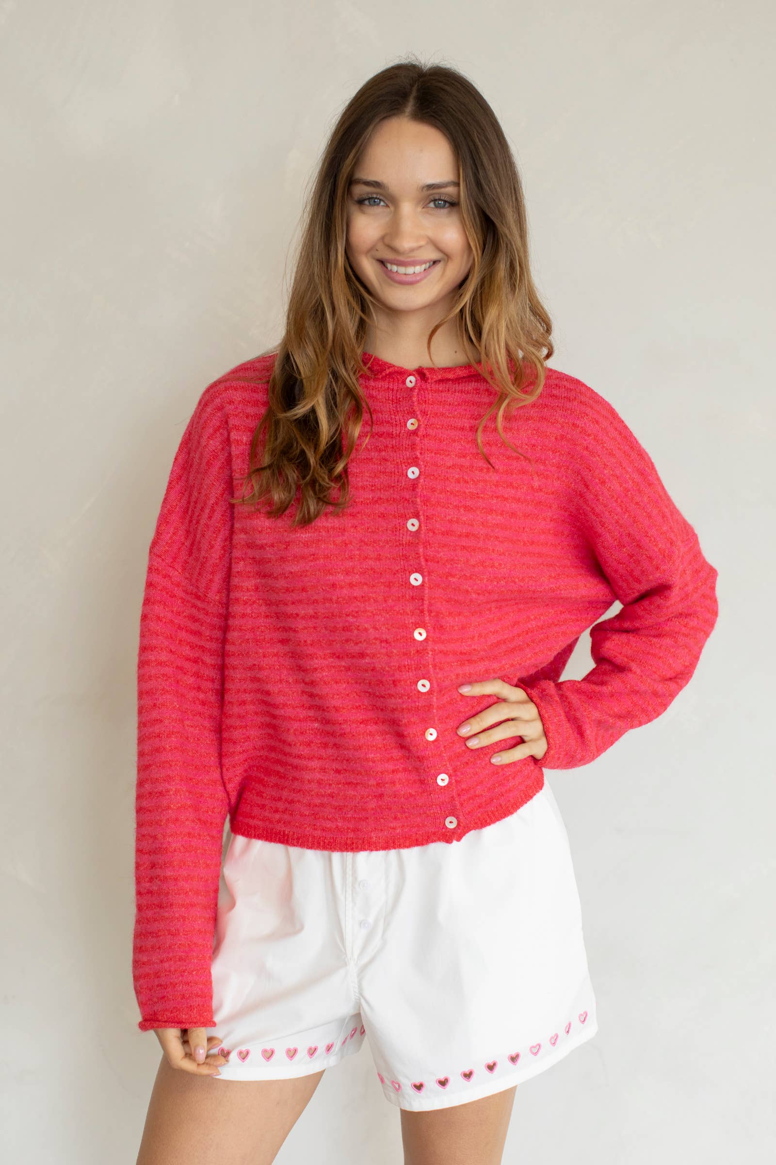 Woman wearing a red textured shirt and white shorts with heart patterns against a plain background