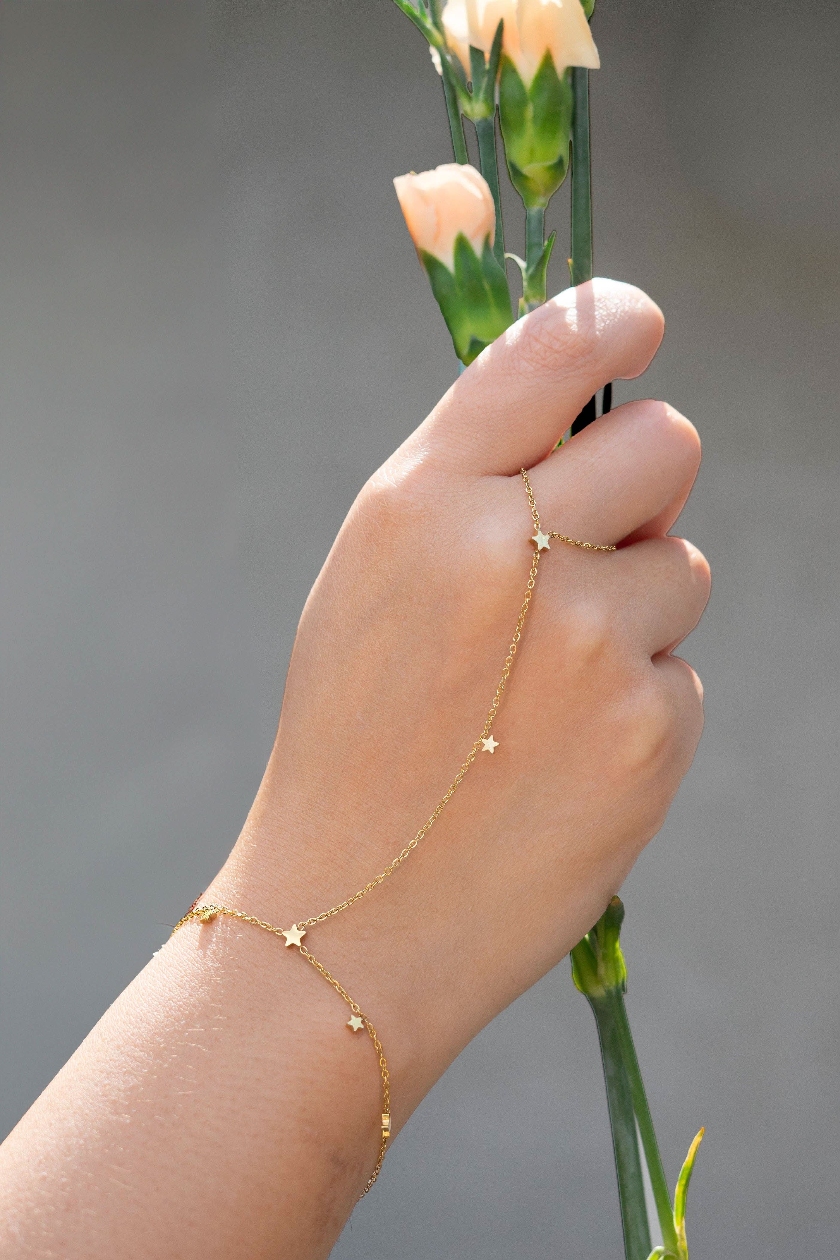 Hand wearing a delicate gold hand chain bracelet connected to a thin ring