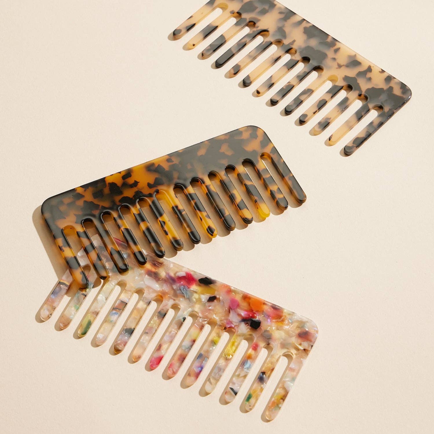 Three combs laying flat on white background in colors- light tortoise, dark tortoise, and confetti tortoise 