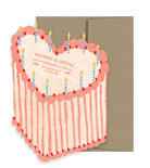 Light pink and red heart shaped happy birthday cake card with candles on top and a brown envelope behind it. 