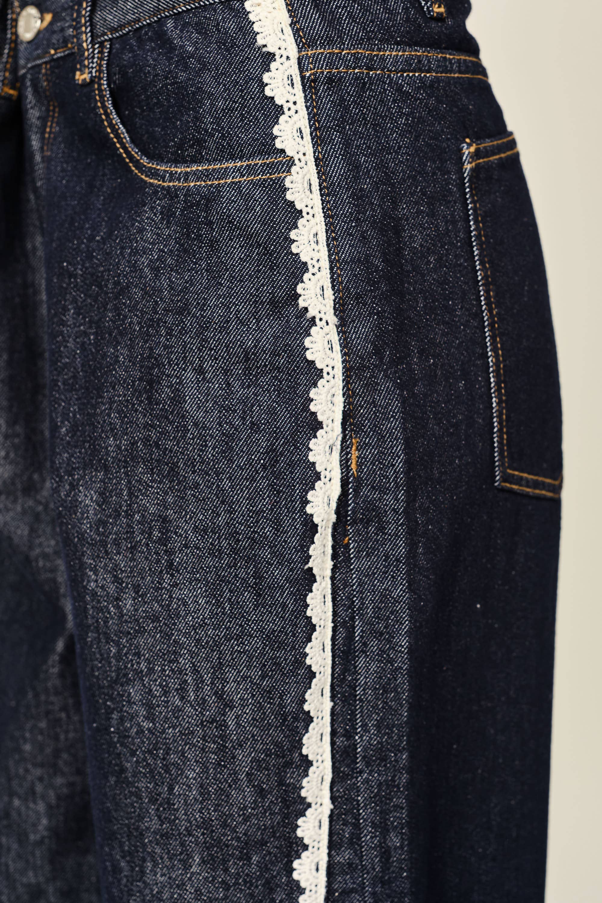 Dark blue jeans with white lace trim on a beige background