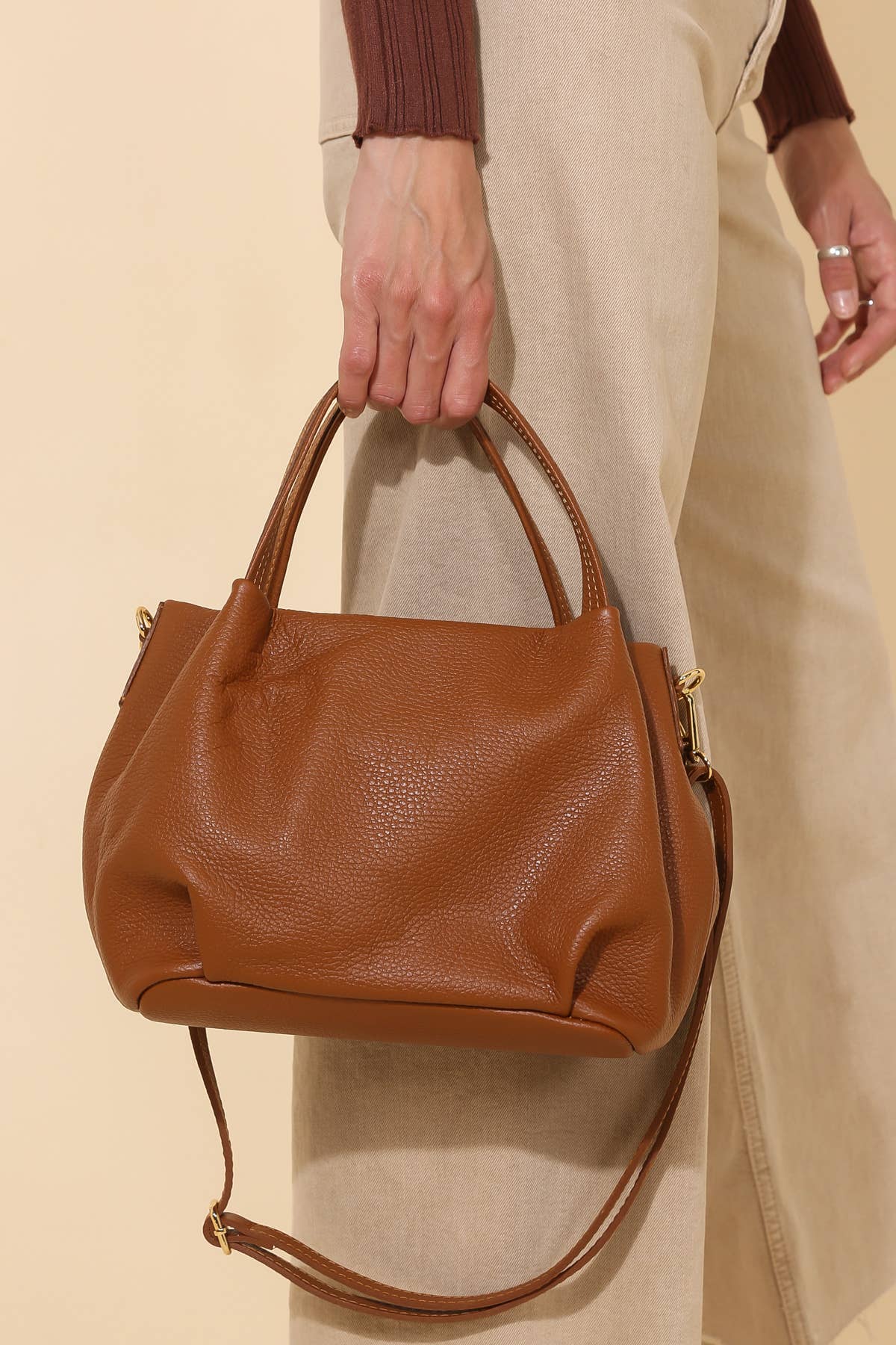 Model holding Big chestnut brown leather handbag purse with handles, strap, and gold details 