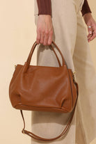Model holding Big chestnut brown leather handbag purse with handles, strap, and gold details 