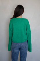 Woman facing away from the camera wearing jeans and a dark Kelly green button up cardigan