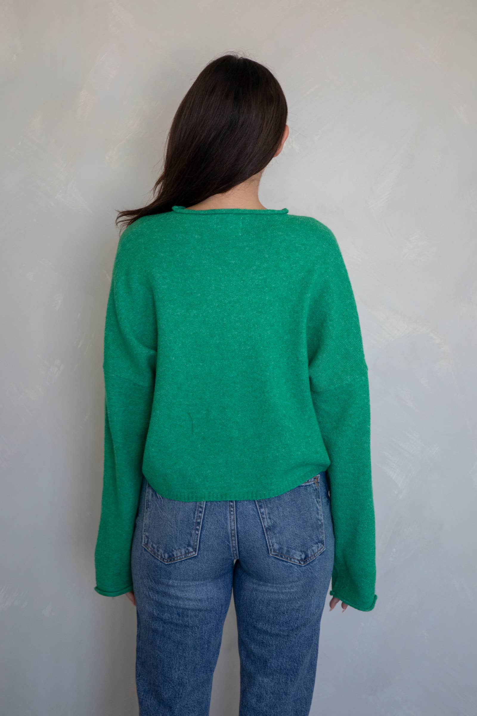Woman facing away from the camera wearing jeans and a dark Kelly green button up cardigan