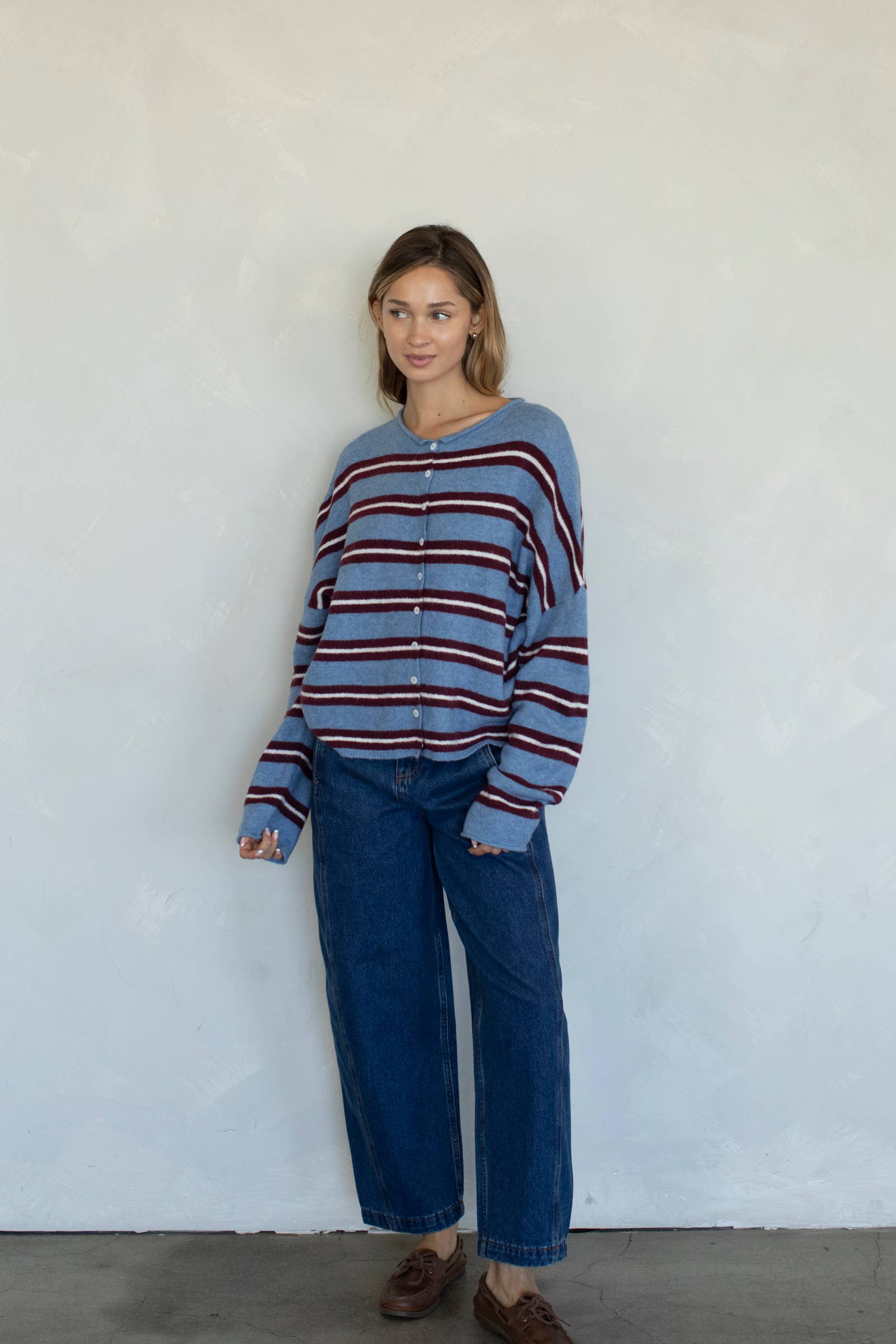 Person wearing a striped sweater and blue jeans against a white wall
