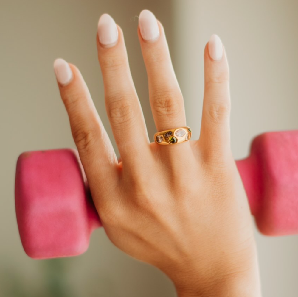 Gold ring with multi shaped and colored gems across the thickest head of the ring 