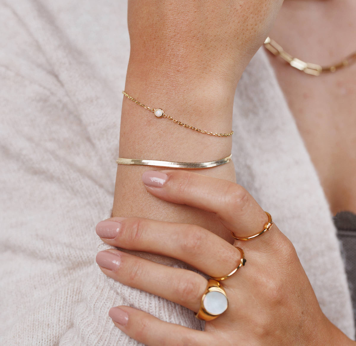 Close-up of a hand wearing gold bracelets and rings on a neutral background