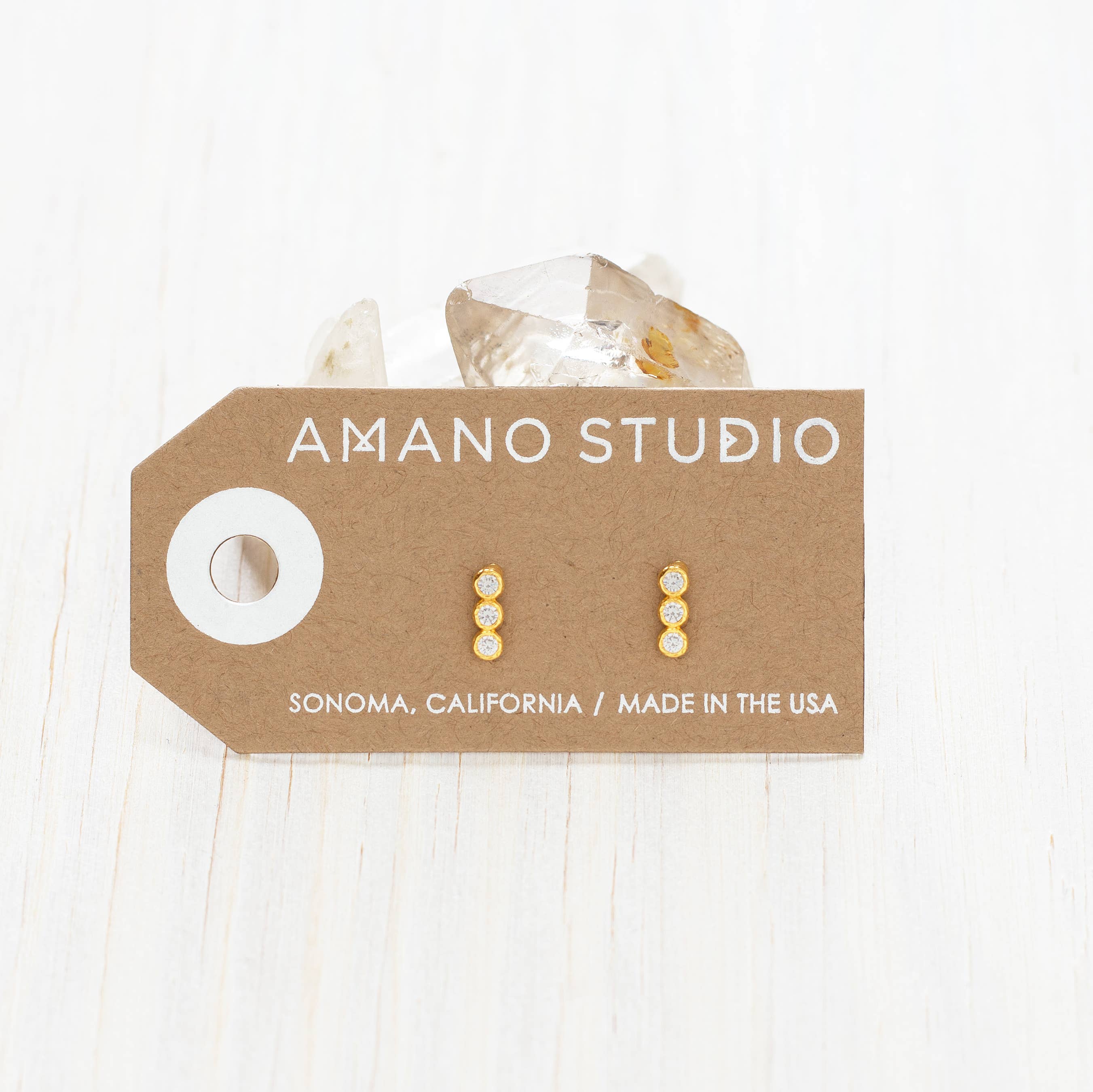 Amano Studio earrings on a branded card with crystals in the background