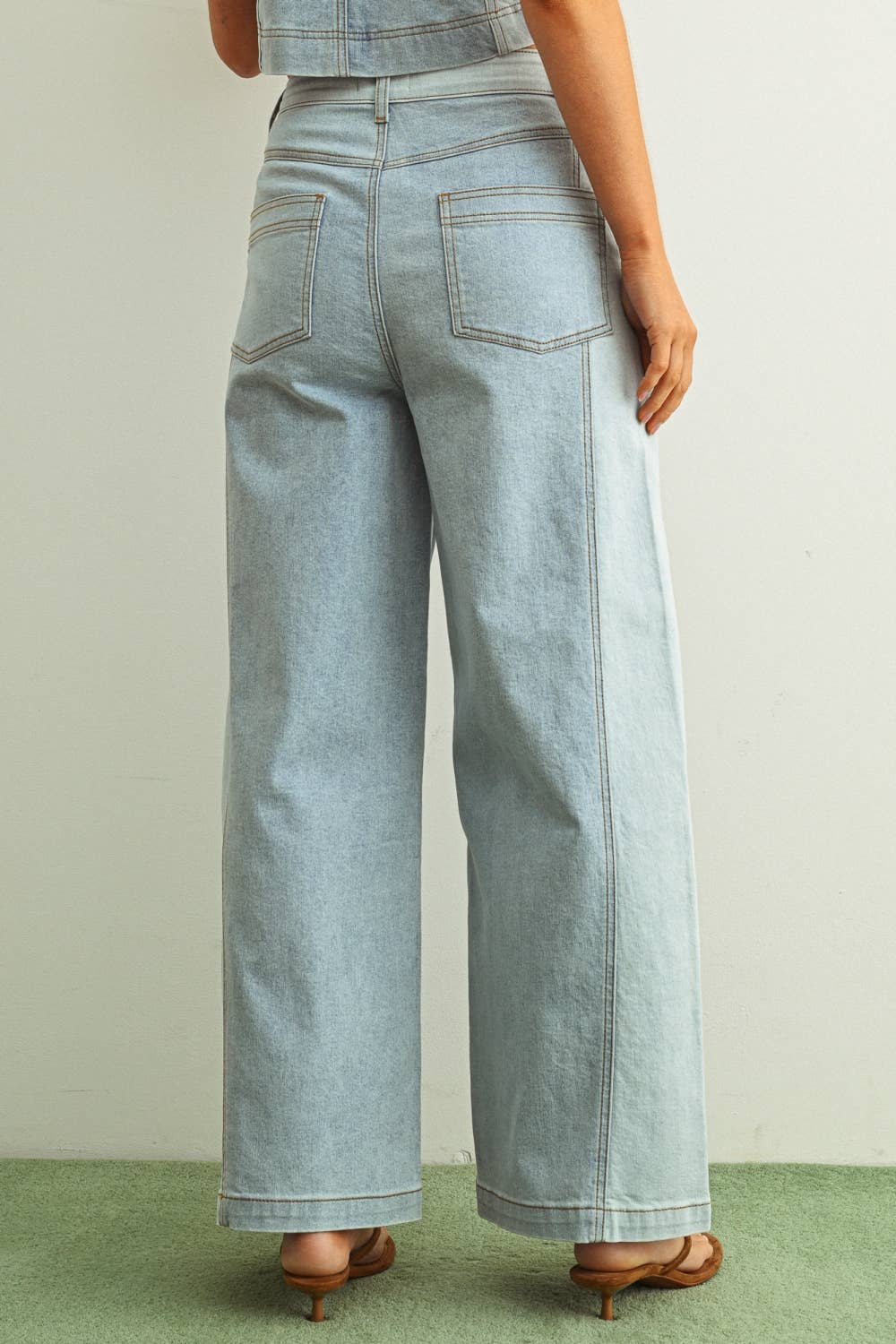 Woman wearing light denim jeans and light brown shoes standing behind a white background