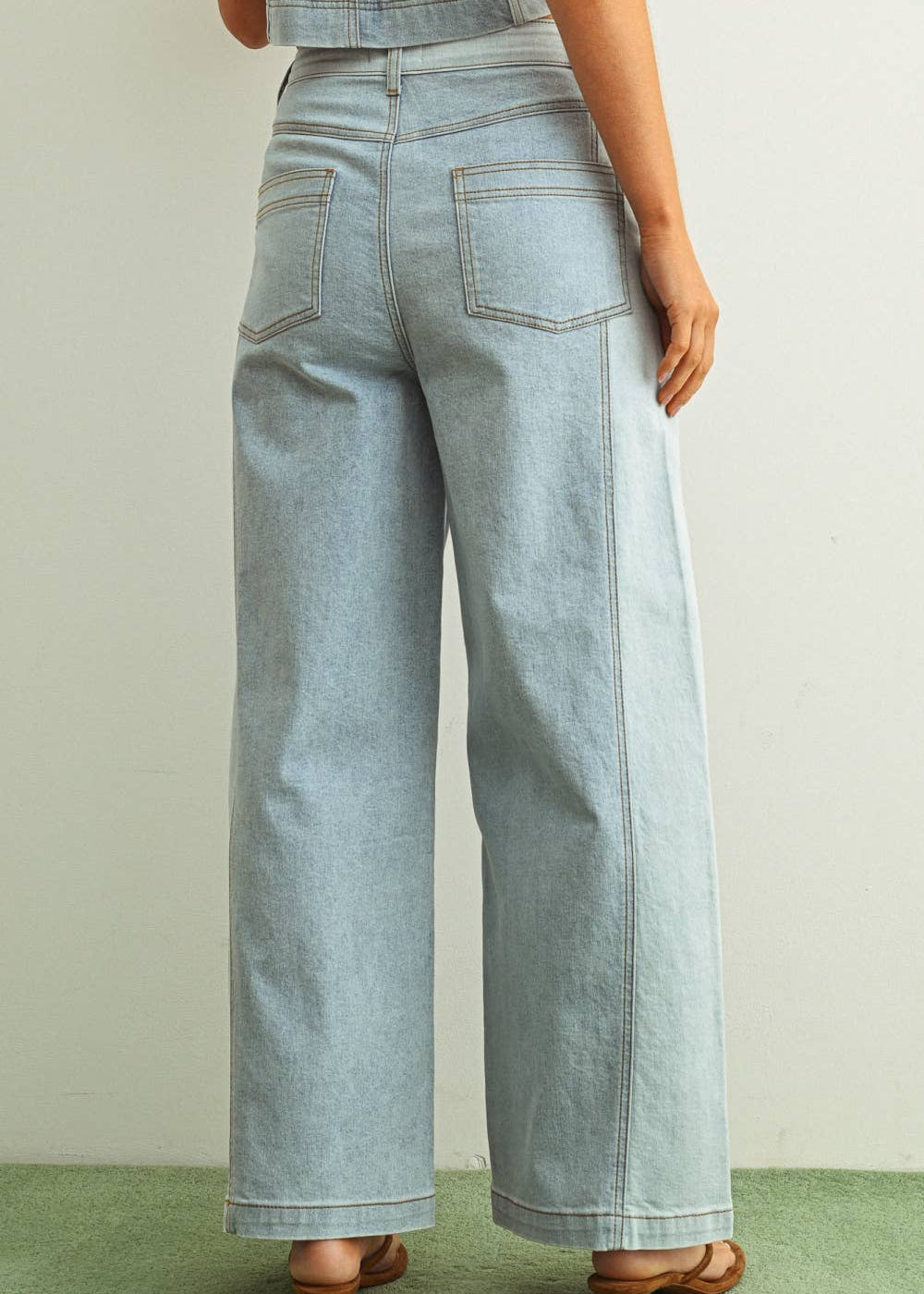 Woman wearing light denim jeans and light brown shoes standing behind a white background