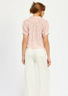 Mdodel standing against a white background wearing white jeans and a pink flowy blouse with tulip embroidery details