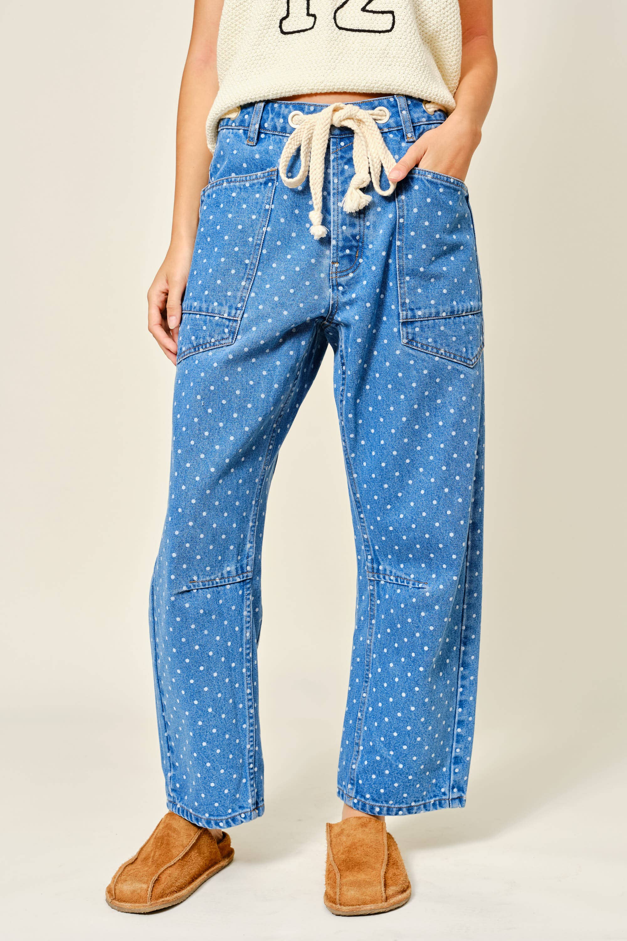 Person wearing blue polka dot pants with a white top and brown shoes on a beige background