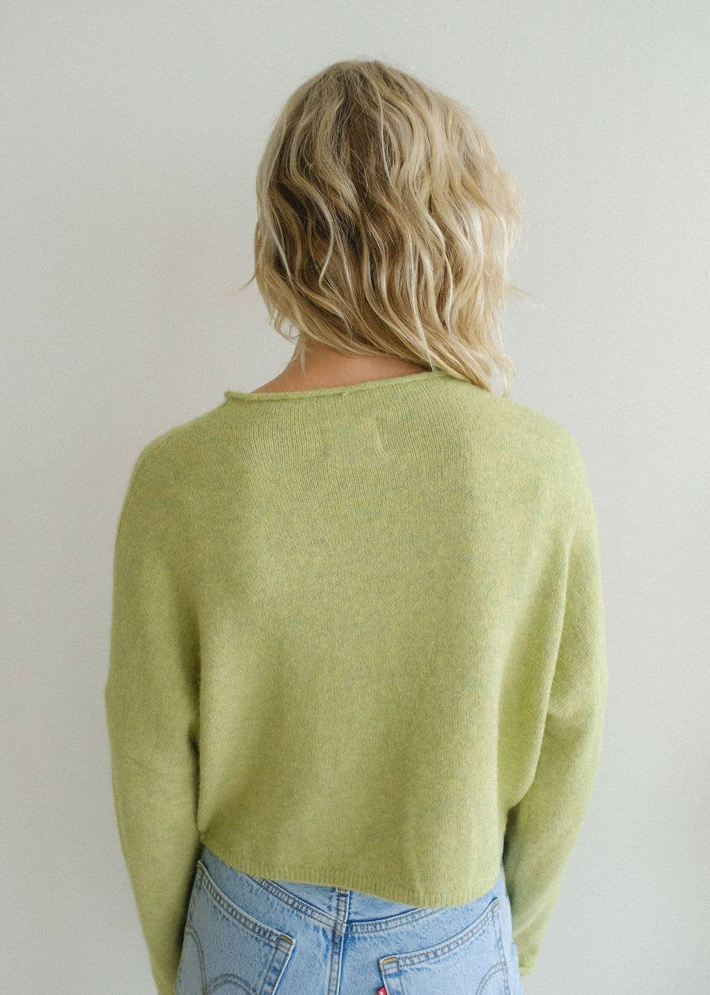 Woman with blonde hair turned backward wearing lemongrass colored cardigan 