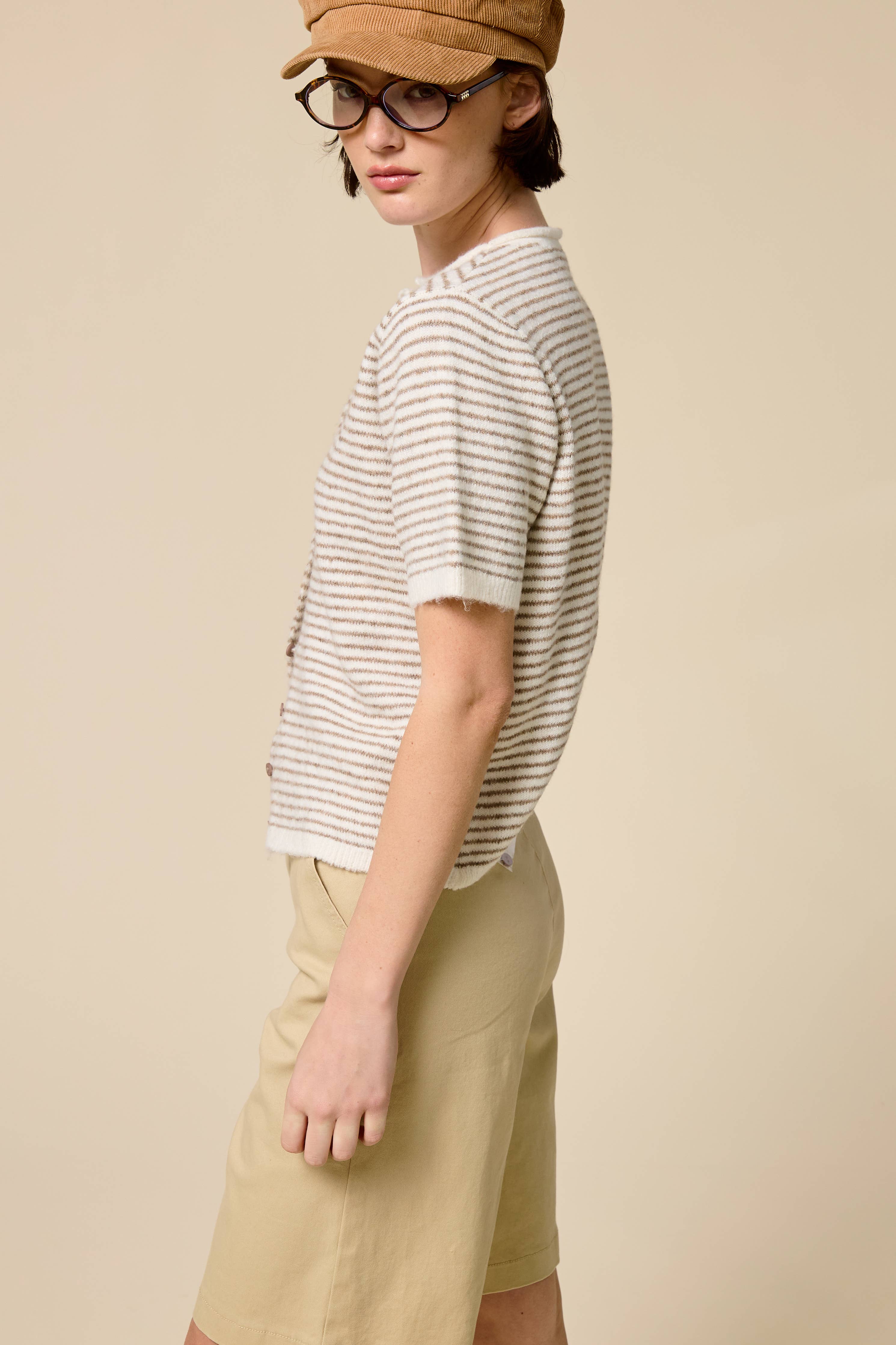 Person wearing a striped shirt, beige cap, and light-colored pants on a plain background
