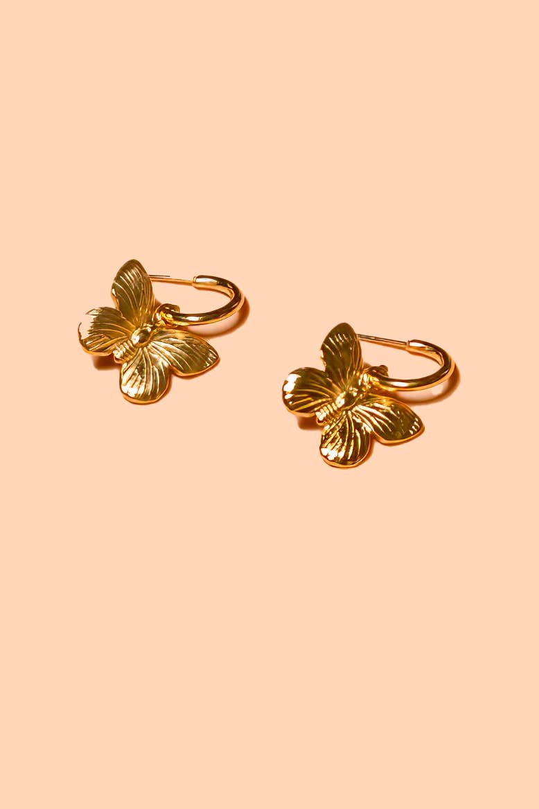 Gold butterfly hoop earring laid flat on a pink background 
