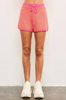 Woman wearing tennis shoes and Candy pink tie waist sweater shorts with pink lining and orange and yellow details 